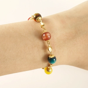 Detail of 18K gold double-layer bracelet with colorful beads and heart charm on wrist