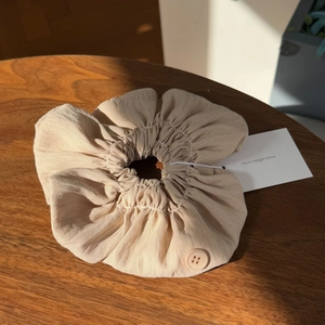 Close-up of cream fabric scrunchie with button detail and soft cotton linen texture