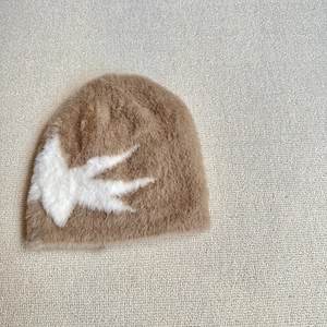 Detail of soft plush knitted beanie featuring a white bird jacquard pattern in light brown