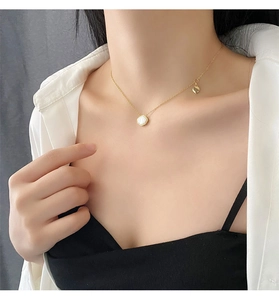 Close-up of a gold titanium shell pendant necklace worn on a female model's collarbone