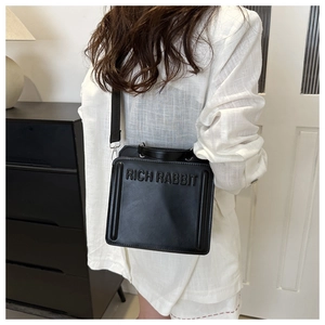 Detail of black PU tote bag with RICH RABBIT embossed text and nylon shoulder strap