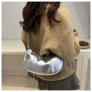 Model wearing silver crescent underarm bag with a glossy metallic finish over camel sweater