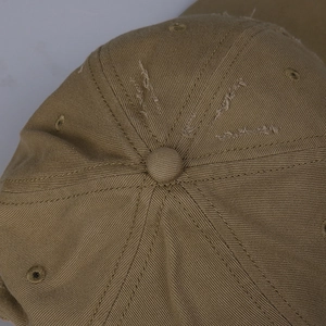Detail of distressed cotton baseball cap showing khaki fabric texture and worn hole effect