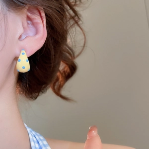 Close-up of a yellow enamel teardrop earring with blue polka dots on a model's ear