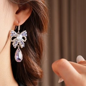 Close-up of elegant bow-shaped earrings featuring a purple teardrop crystal pendant