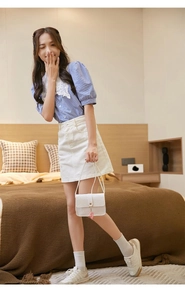Close-up of white embossed handbag with heart pendant and floral lace collar top