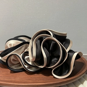 Detail of a large satin scrunchie with layered black and beige wavy ruffles on wood