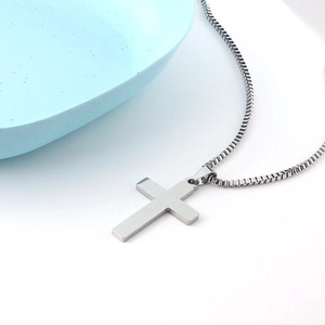 Macro shot of silver stainless steel cross pendant with venetian box chain on white surface