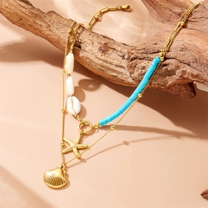 Double-layered gold necklace featuring starfish and shell pendants on a warm sandy background
