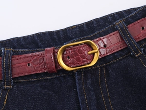 Détail de la ceinture croco bordeaux avec boucle dorée sur un jean bleu foncé