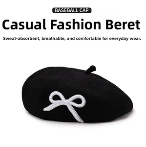Detail of a black knit beret featuring a white embroidered bow and small top tail