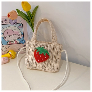 Detail of hand-woven straw bag with red plush strawberry decor and woven shoulder strap