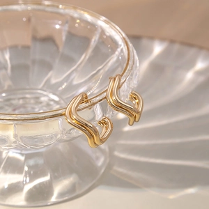 Macro shot of gold geometric wavy earrings hanging on a textured transparent glass rim