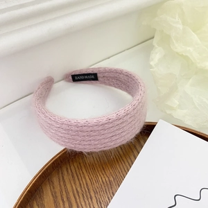 Close-up of pink plush knitted headband with handmade label on wooden tray