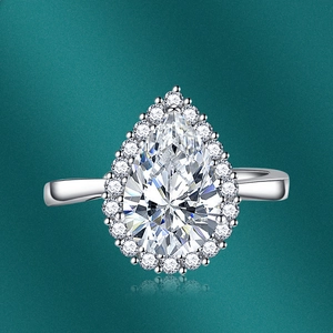 Macro shot of pear-cut emerald gemstone ring with halo diamond setting on green background