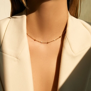 Detailed view of minimalist 18K gold-plated beaded chain worn over a beige suit