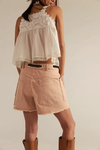 Detail of pink denim shorts featuring back pockets and raw frayed hem on a model
