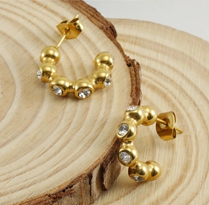 Macro detail of 18K gold-plated C-shaped earrings with clear zircons on wooden background