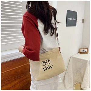 Detail of beige canvas crossbody bag featuring a cartoon eye print and shh text