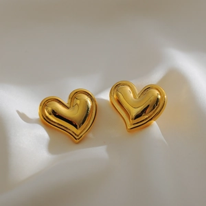 Macro shot of polished gold heart-shaped stud earrings on white silk fabric background
