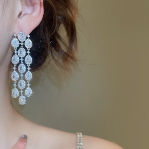 Macro shot of dangling silver earrings with cubic zirconia tassels on a female model