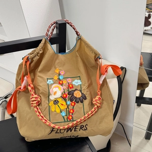 Detail of khaki nylon tote bag featuring colorful floral embroidery and braided orange straps