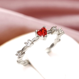Macro shot of a red heart-shaped gemstone ring with side zircon on pink silk fabric
