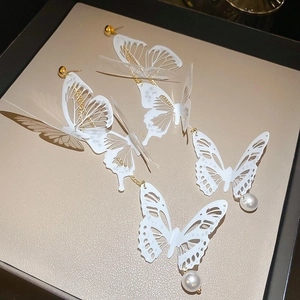 Détail de boucles d'oreilles papillon en acrylique blanc avec perles et liens dorés