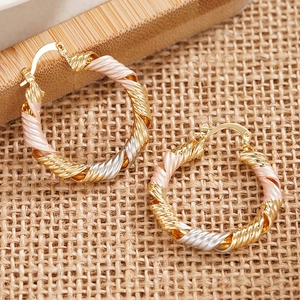 Macro detail of tricolor gold twisted hoop earrings with elegant spiral rope texture