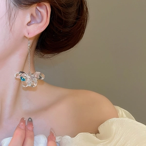Detail of a butterfly acrylic drop earring with a blue stone accent on a female model