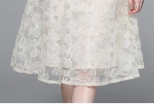 Details eines beigen Kleides mit zarter Blumenspitze und schimmernden Pailletten