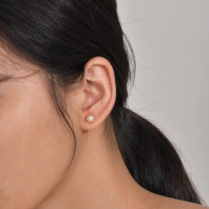 Close-up of minimalist white round pearl stud earrings with gold base worn on ear