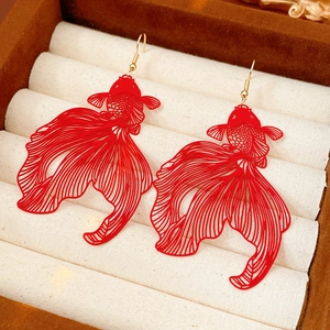 Gros plan sur des boucles d'oreilles carpe koï rouges avec détails ajourés sur coussin