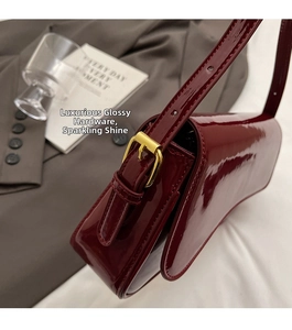 Close-up of glossy burgundy patent leather bag with adjustable golden metal buckle detail