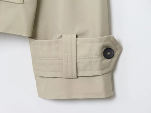 Detail shot of khaki trench coat cuff with textured twill fabric and dark button strap
