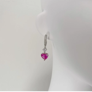 Détail d'une boucle d'oreille argentée avec pierre claire et pendentif coeur rose