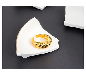 Macro detail of golden croissant twist ring on white stone texture, minimalist style