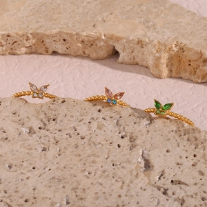 Detailaufnahme von drei goldenen Schmetterlingsringen mit bunten Edelsteinen auf Steinen