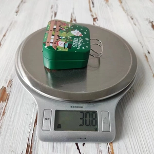 Close-up of green Christmas tin box showing 30.8g weight on a digital scale