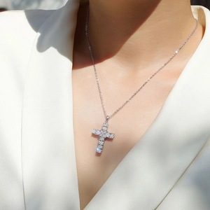 Close-up of 925 silver cross necklace with pavé-set stones on a model in white blazer