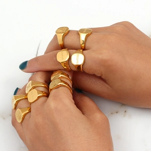 Detail of 18K gold-plated signet rings with engraved quotes on marble background