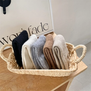 Close-up of five pairs of thick knit winter socks in neutral tones inside a woven basket