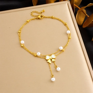 Detail of double-layer gold plated bracelet featuring white pearls and a bow charm