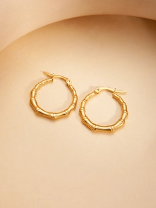 Close-up of golden bamboo-style hoop earrings with vintage texture on a beige stand