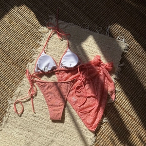 Detailed flat lay of pink floral lace 3-piece bikini set with matching sarong wrap skirt