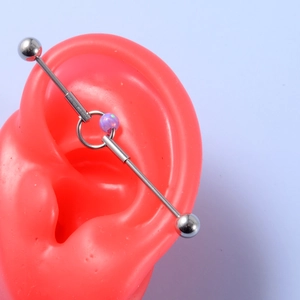 Macro shot of silver industrial barbell with purple opal bead on silicone ear model