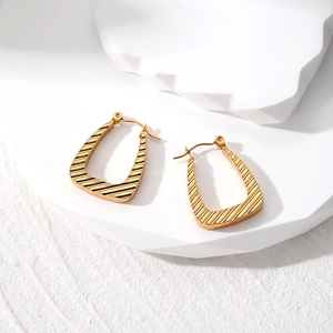 Detailed view of golden geometric earrings with textured diagonal stripes on white stand