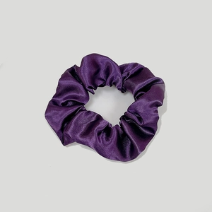 Macro shot of dark purple satin scrunchie showing glossy texture and pleats