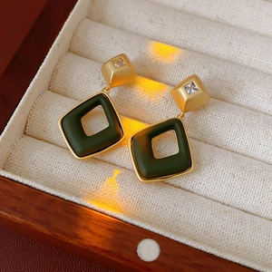 Macro shot of gold geometric earrings with emerald green stones on beige velvet