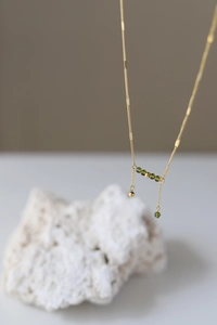 Detail of elegant gold chain with olive green crystals and asymmetric hanging tassels